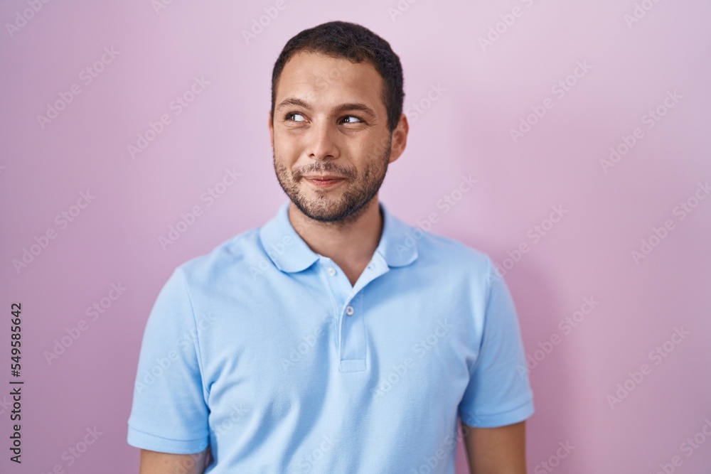 Hispanic man standing over pink background smiling looking to the side and staring away thinking. Hispanic man standing over pink background smiling looking to the side and staring away thinking.