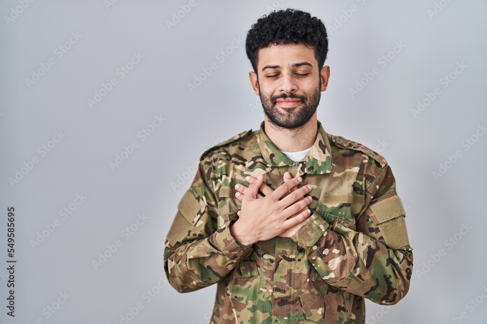 Arab man wearing camouflage army uniform smiling with hands on chest with closed eyes and grateful gesture on face. health concept.