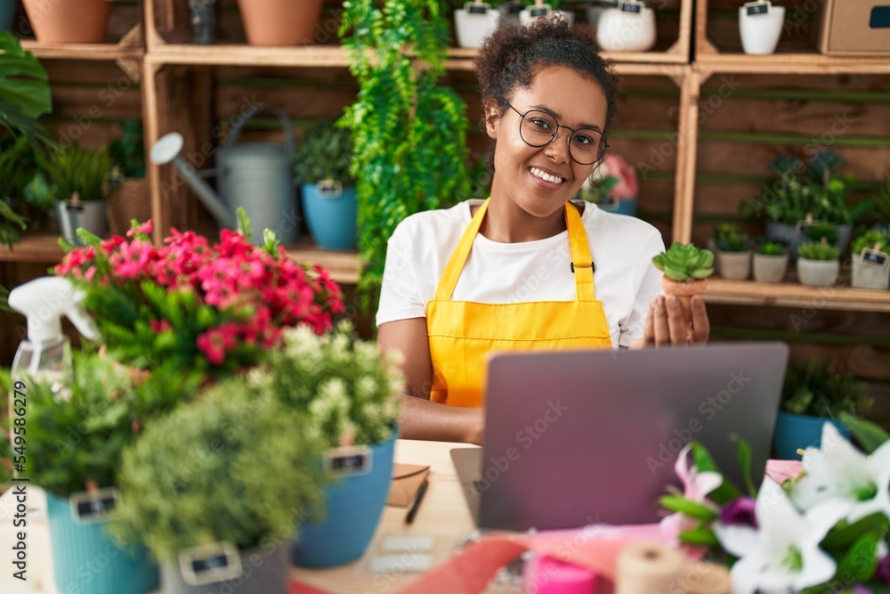 African american woman florist using laptop holding plant at flower shop African american woman florist using laptop holding plant at flower shop