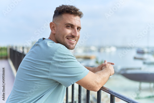 Young hispanic man smiling confident leaning on balustrade at seaside