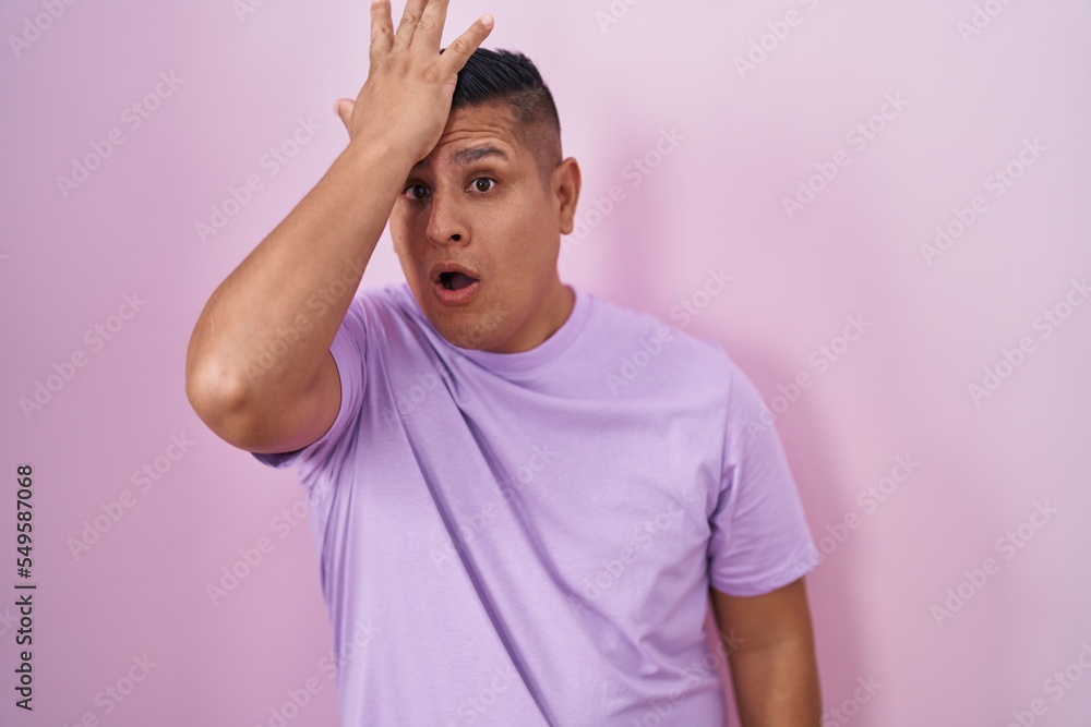 Young hispanic man standing over pink background surprised with hand on head for mistake, remember error. forgot, bad memory concept. Young hispanic man standing over pink background surprised with hand on head for mistake, remember error. forgot, bad memory concept.