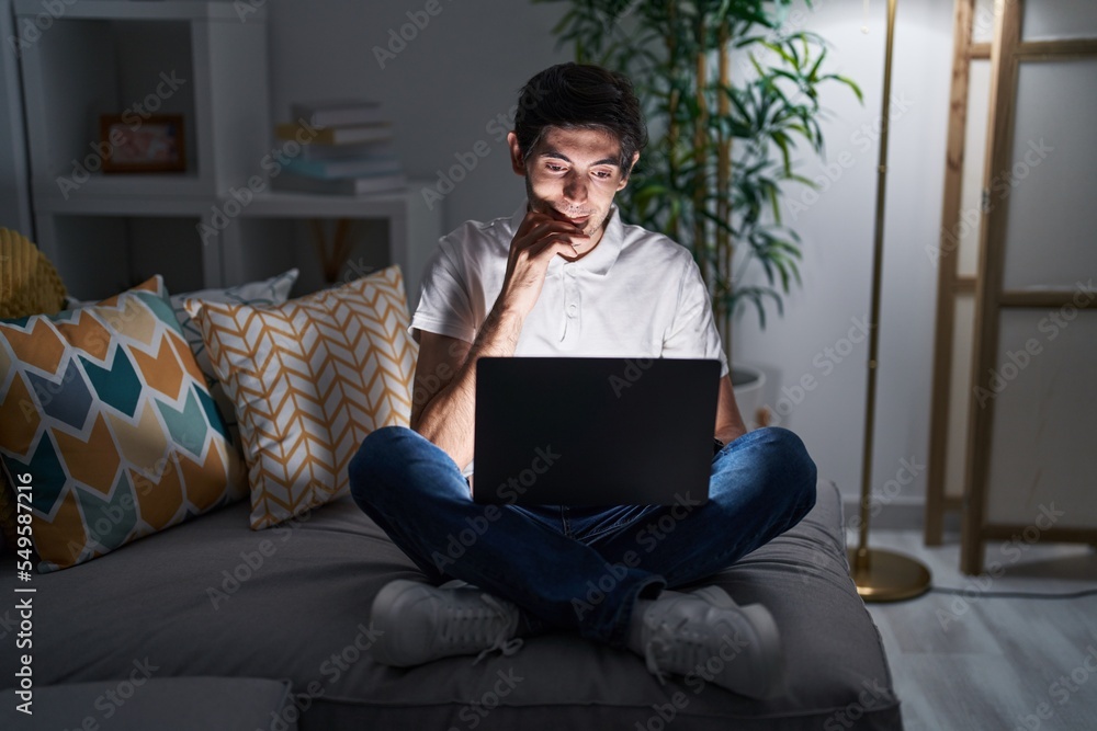 Young hispanic man using laptop at home at night looking stressed and nervous with hands on mouth biting nails. anxiety problem. Young hispanic man using laptop at home at night looking stressed and nervous with hands on mouth biting nails. anxiety problem.