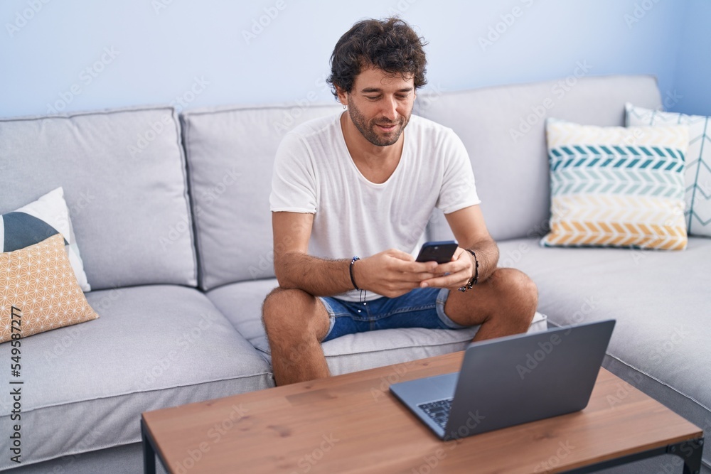 Young hispanic man using smartphone and laptop at home Young hispanic man using smartphone and laptop at home