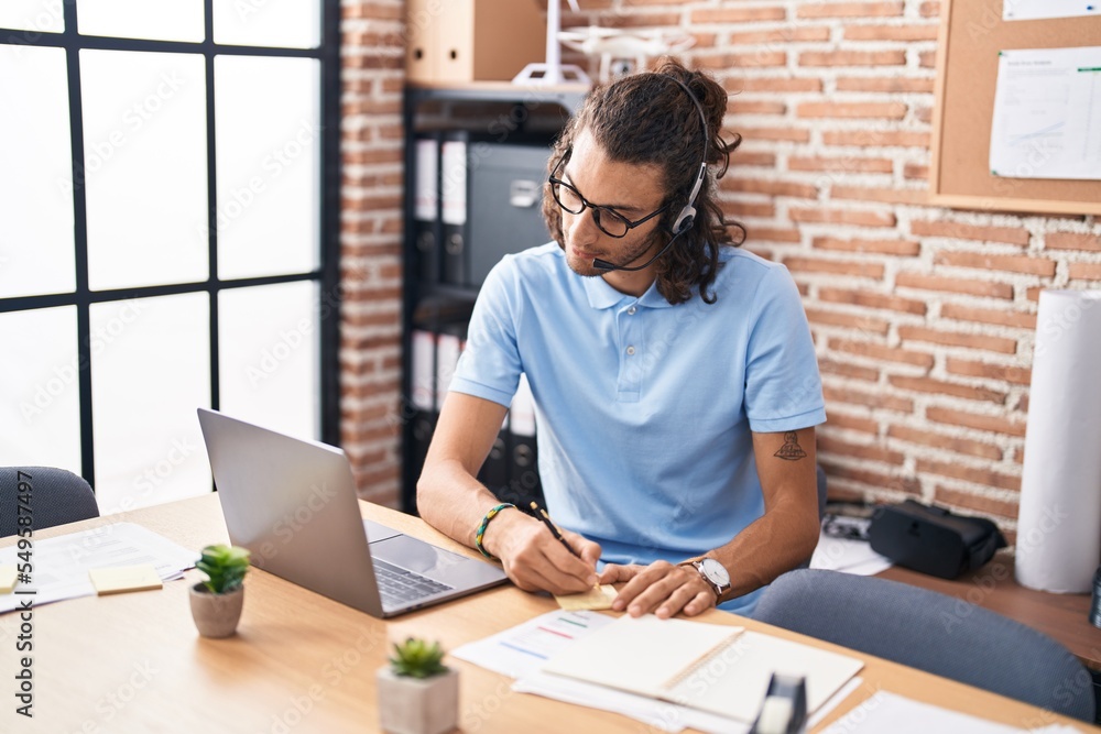 Young hispanic man call center agent writing on reminder paper at office Young hispanic man call center agent writing on reminder paper at office