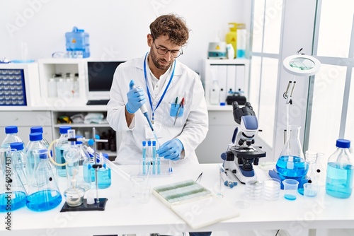 Young hispanic man wearing scientist uniform working at laboratory