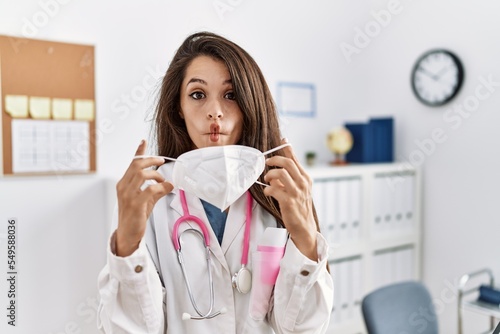 Young doctor woman wearing safety mask at the clinic making fish face with mouth and squinting eyes  crazy and comical.