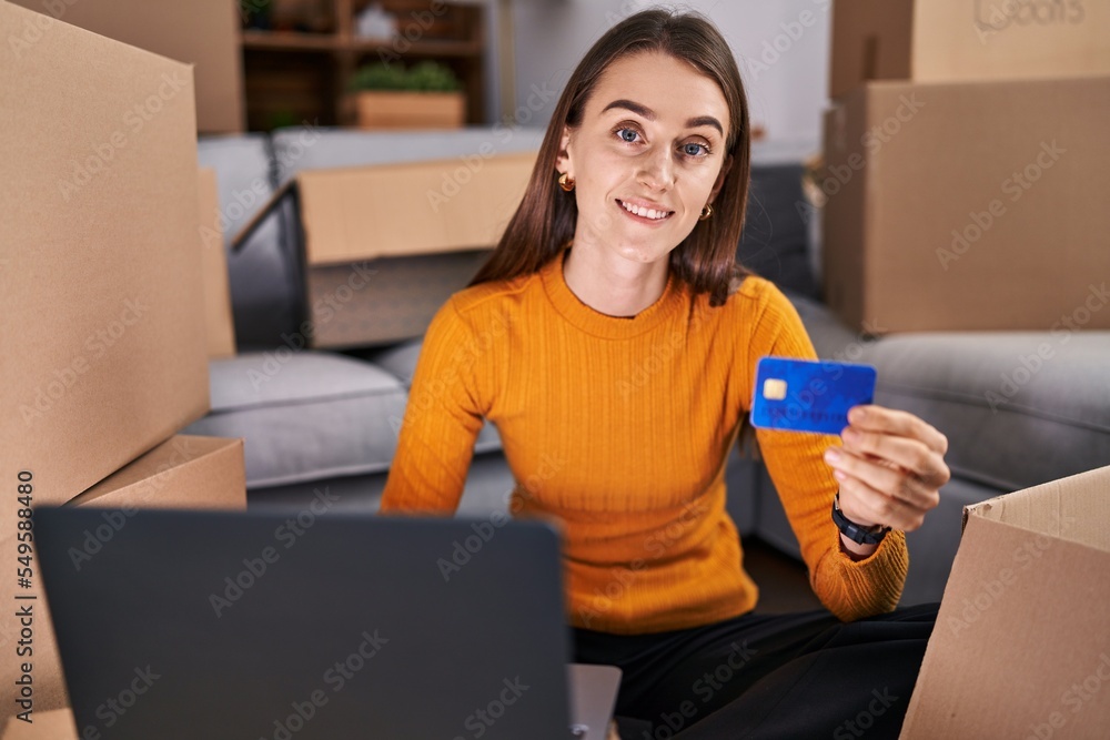 Young caucasian woman using laptop and credit card sitting on floor at new home Young caucasian woman using laptop and credit card sitting on floor at new home