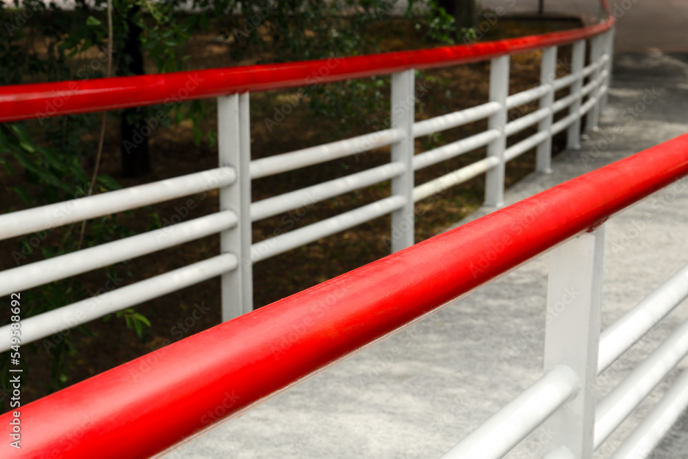 Ramp with red metal handrailings near trees outdoors
