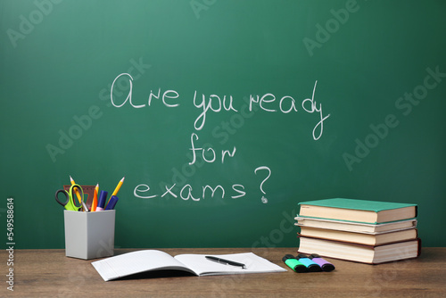 Different stationery and books on wooden table near chalkboard with phrase Are You Ready For Exams