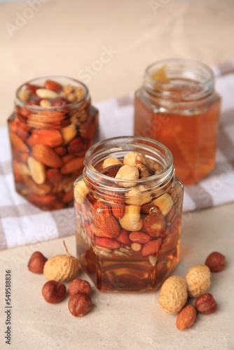 Jars with different nuts and honey on beige table