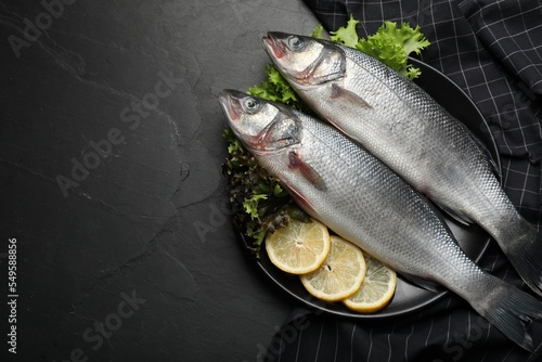 Fresh raw sea bass fish and ingredients on black table, top view. Space for text