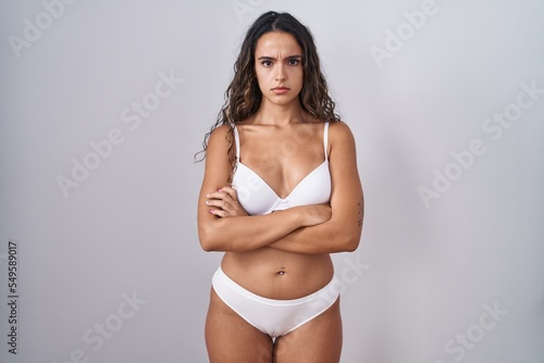 Young hispanic woman wearing white lingerie skeptic and nervous, disapproving expression on face with crossed arms. negative person.