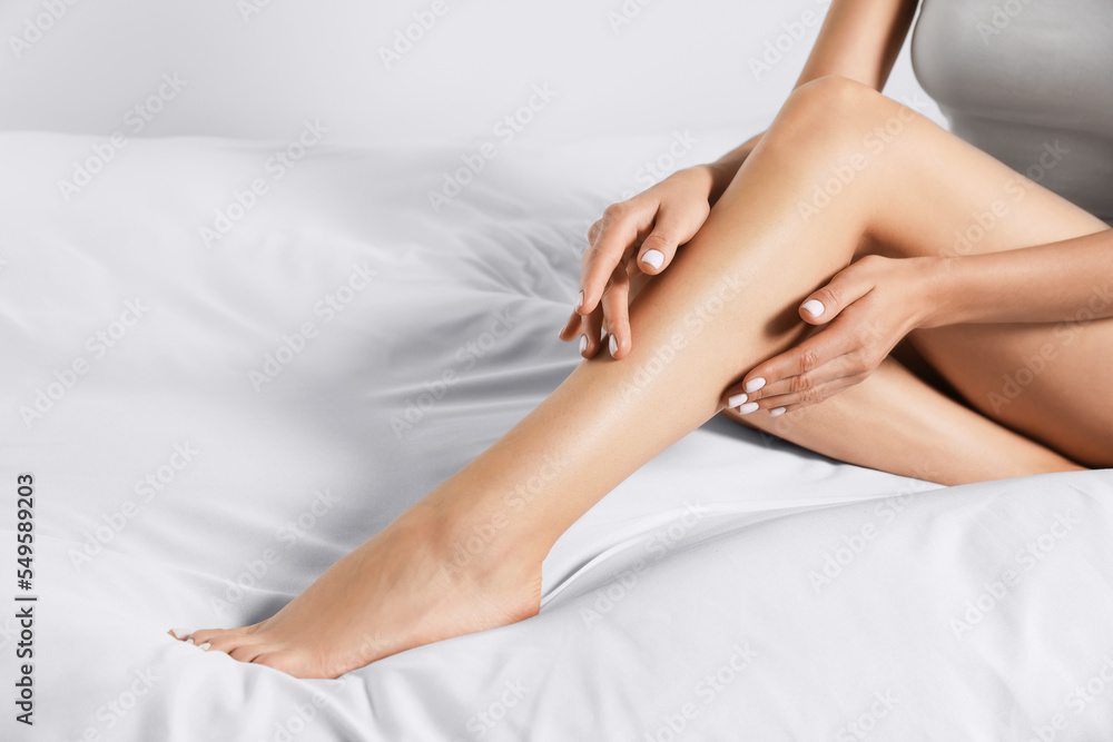 Woman with beautiful long legs sitting on bed at home, closeup Woman with beautiful long legs sitting on bed at home, closeup