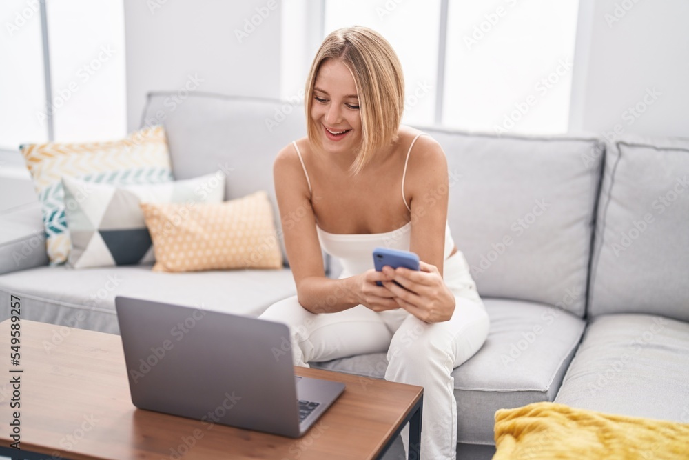 Young blonde woman using laptop and smartphone at home Young blonde woman using laptop and smartphone at home