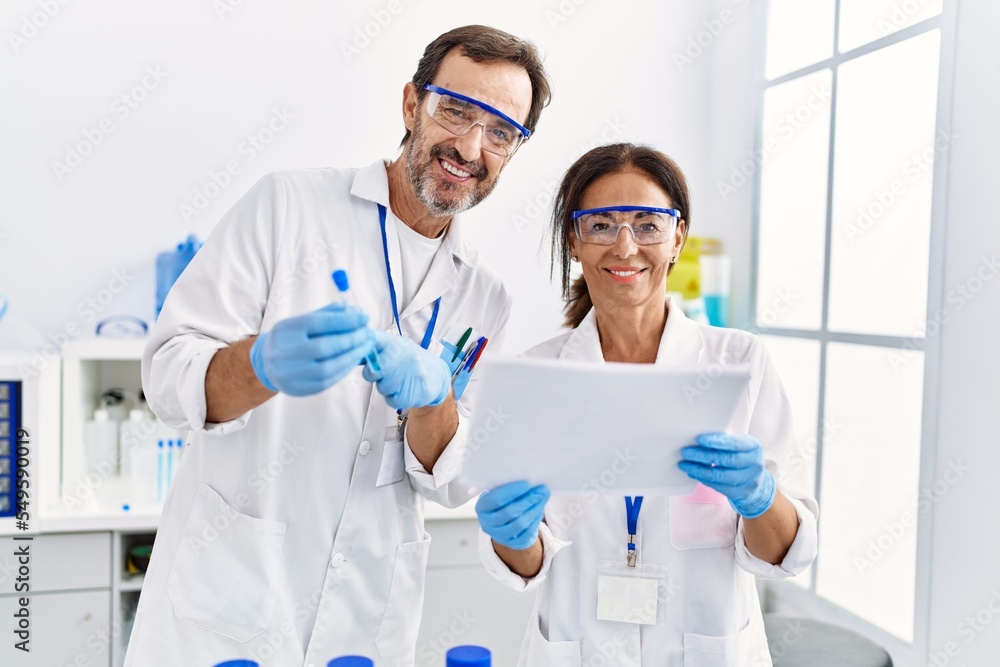 Middle age man and woman partners wearing scientist uniform reading document and holding test tube at laboratory Middle age man and woman partners wearing scientist uniform reading document and holding test tube at laboratory