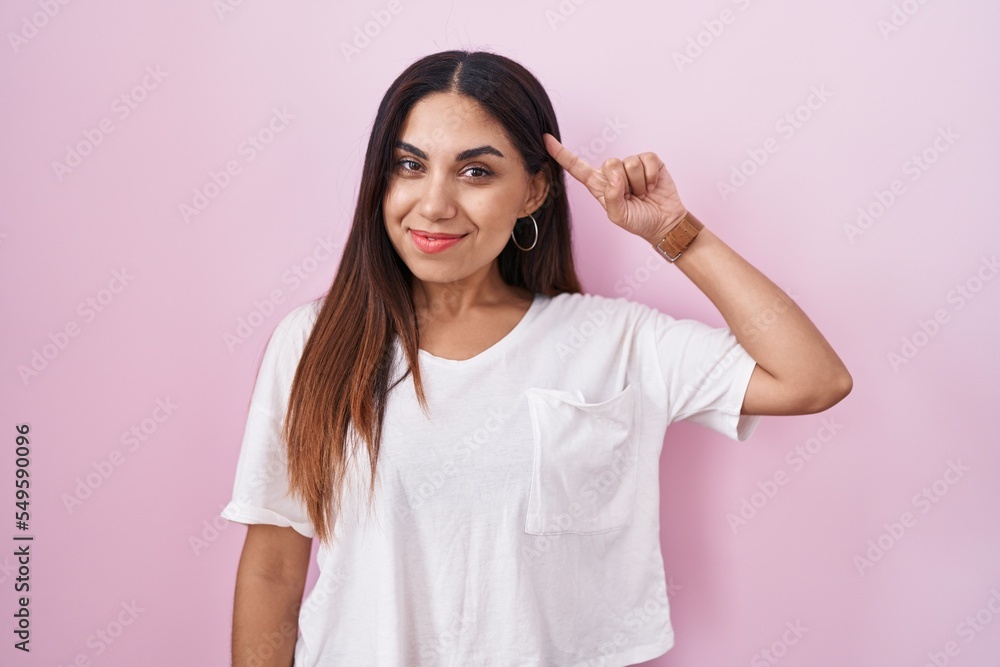 Young arab woman standing over pink background smiling pointing to head with one finger, great idea or thought, good memory