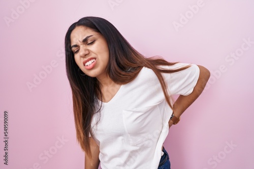 Young arab woman standing over pink background suffering of backache, touching back with hand, muscular pain