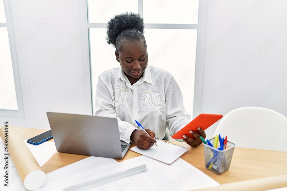 Young african american woman architect using touchpad writing on notebook at architecture studio Young african american woman architect using touchpad writing on notebook at architecture studio