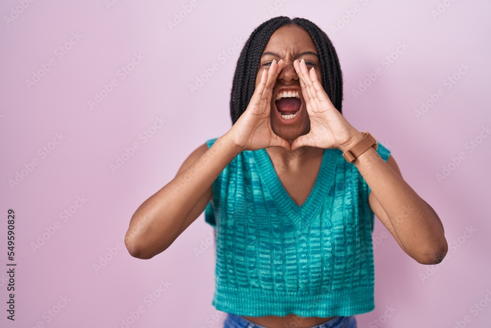 Young african american with braids standing over pink background shouting angry out loud with hands over mouth Young african american with braids standing over pink background shouting angry out loud with hands over mouth