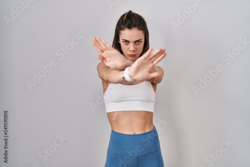 Hispanic woman wearing sportswear over isolated background rejection expression crossing arms and palms doing negative sign, angry face