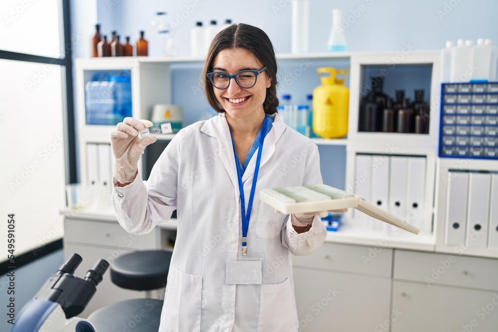 Young hispanic woman working at scientist laboratory with blood samples winking looking at the camera with sexy expression, cheerful and happy face. Young hispanic woman working at scientist laboratory with blood samples winking looking at the camera with sexy expression, cheerful and happy face.