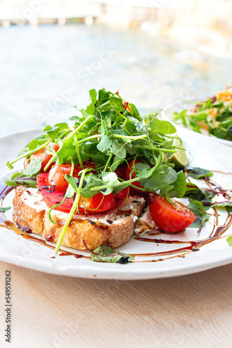 Tasty savory tomatoes on slices of toasted and young green sprouts of peas garnished on wooden table in a café with view on beach at day sun light on background.