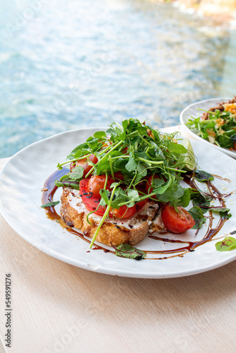 Tasty savory tomatoes on slices of toasted and young green sprouts of peas garnished on wooden table in a café with view on beach at day sun light on background.