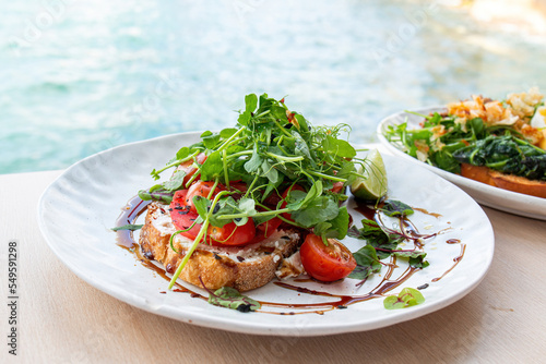 Tasty savory tomatoes on slices of toasted and young green sprouts of peas garnished on wooden table in a café with view on beach at day sun light on background.