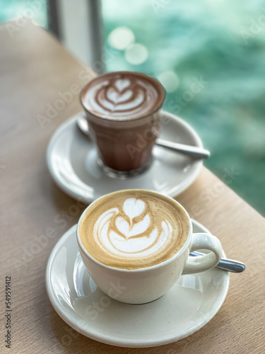 Close up Cup of fresh coffee with latte art on wooden table in a café with view on beach at day sun light on background.