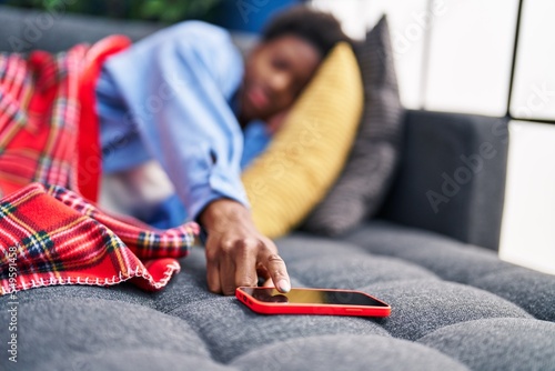 African american woman lying on sofa sleeping turning off smartphone alarm at home