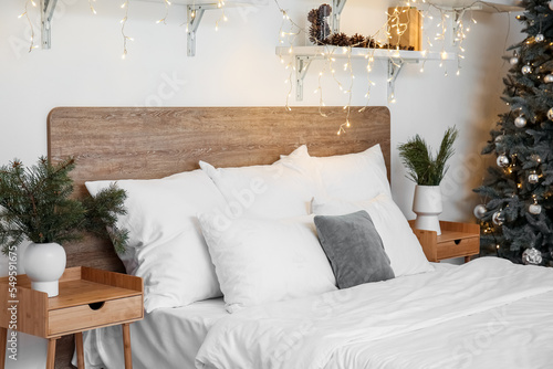 Vases with Christmas branches on tables and bed in bedroom