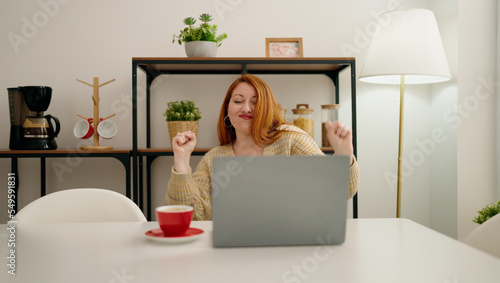 Young redhead woman using laptop with celebrate expression at home