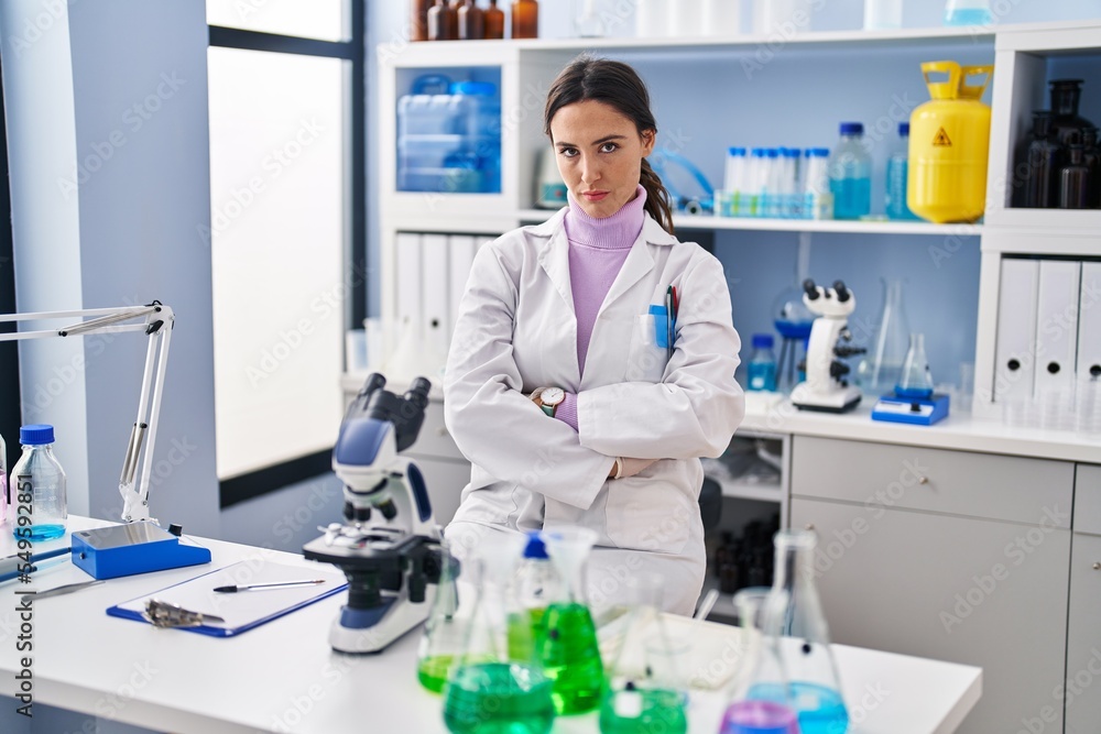 Young brunette woman working at scientist laboratory skeptic and nervous, disapproving expression on face with crossed arms. negative person.
