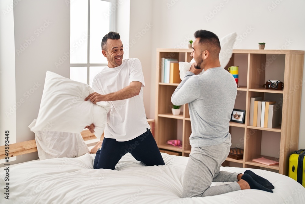 Fototapeta premium Two men couple fighting with pillows at bedroom