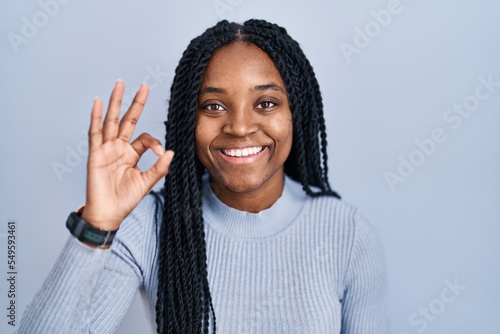 African american woman standing over blue background smiling positive doing ok sign with hand and fingers. successful expression. © Krakenimages.com