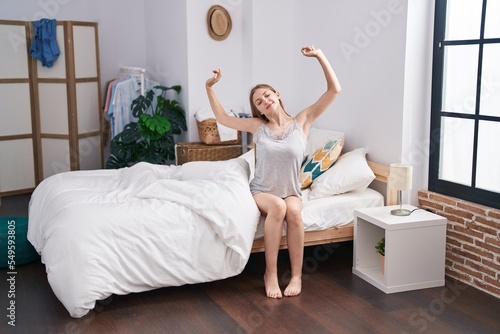 Young caucasian woman waking up stretching arms at bedroom