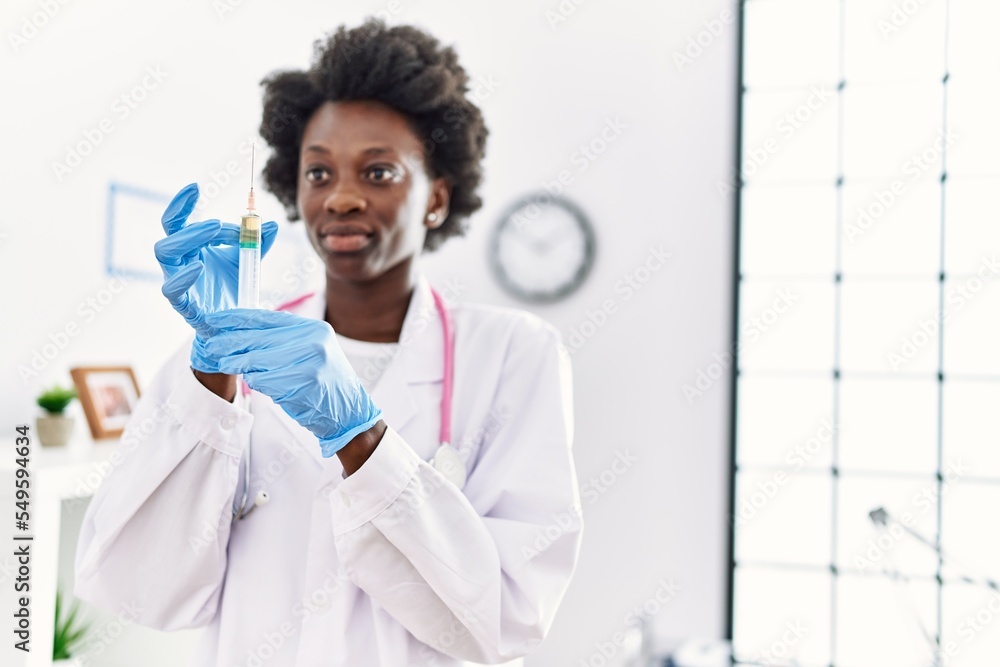 Young african american woman wearing doctor uniform holding syringe at clinic