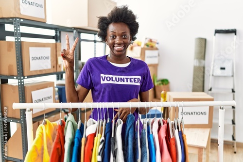 African young woman wearing volunteer t shirt at donations stand showing and pointing up with fingers number two while smiling confident and happy.