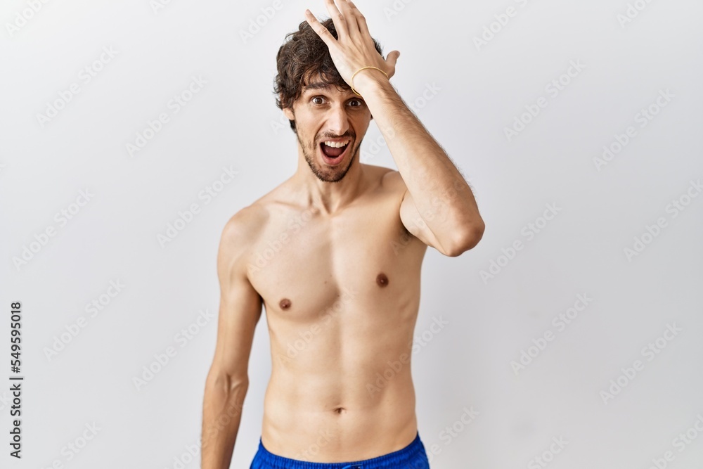 Young hispanic man standing shirtless over isolated, background surprised with hand on head for mistake, remember error. forgot, bad memory concept.