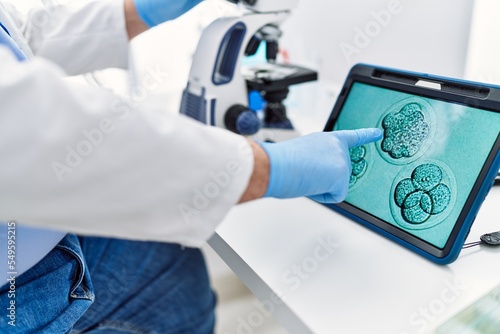 Middle age grey-haired man wearing scientist uniform looking embryology image touchpad at laboratory photo