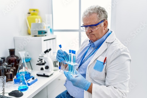 Middle age grey-haired man wearing scientist uniform holding test tube at laboratory