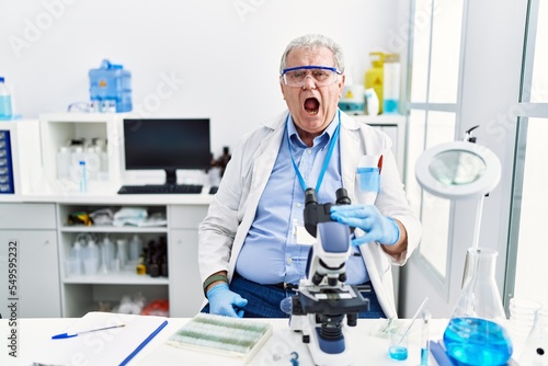 Senior caucasian man working at scientist laboratory angry and mad screaming frustrated and furious  shouting with anger. rage and aggressive concept.