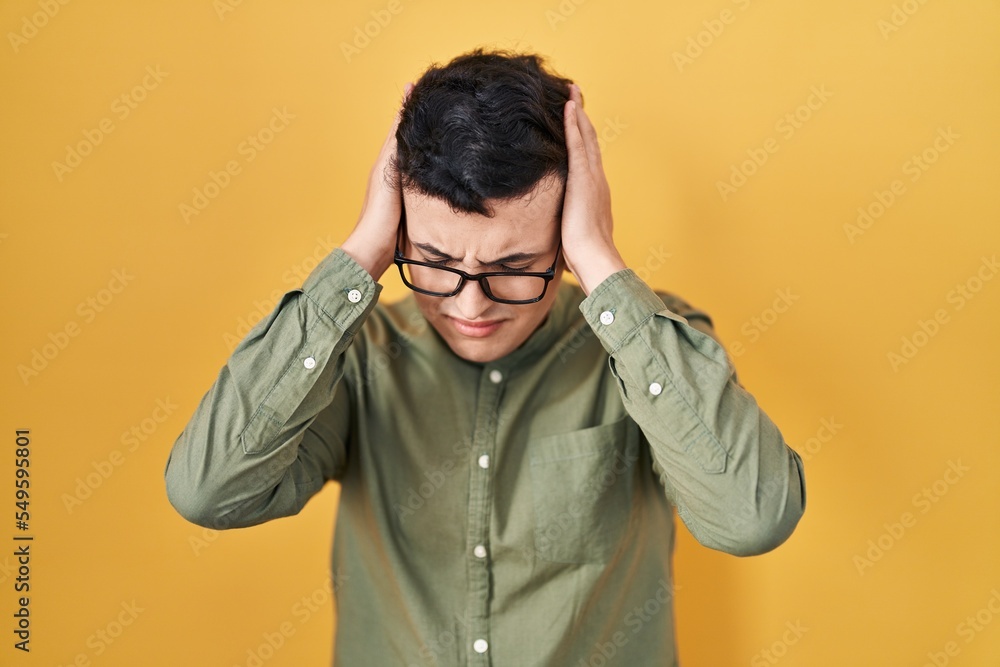 Non binary person standing over yellow background suffering from headache desperate and stressed because pain and migraine. hands on head. Non binary person standing over yellow background suffering from headache desperate and stressed because pain and migraine. hands on head.