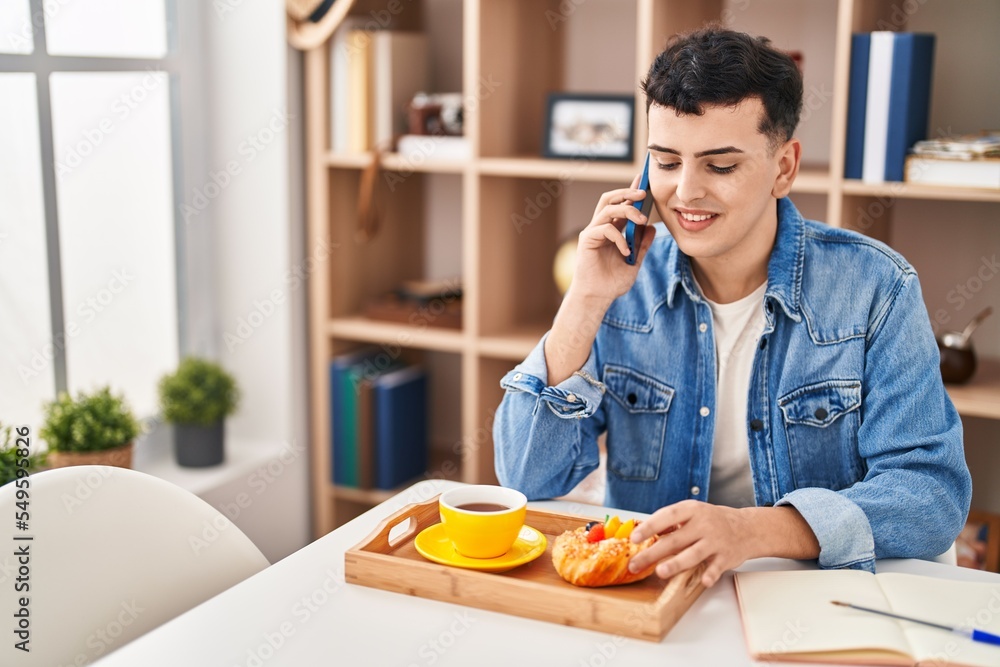 Young non binary man talking on the smartphone having breakfast at home Young non binary man talking on the smartphone having breakfast at home