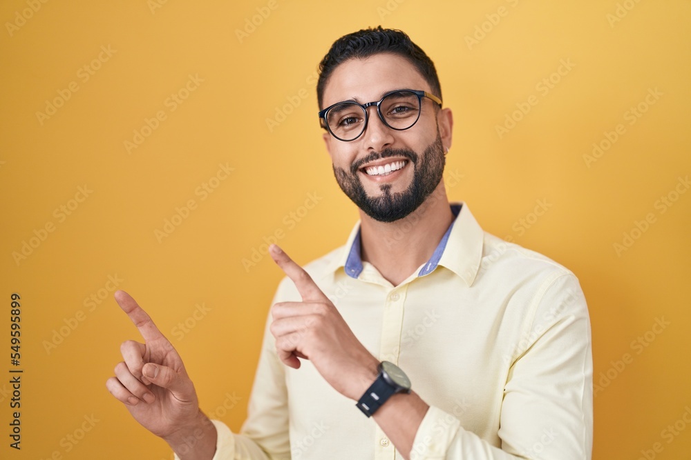 Hispanic young man wearing business clothes and glasses smiling and looking at the camera pointing with two hands and fingers to the side. Hispanic young man wearing business clothes and glasses smiling and looking at the camera pointing with two hands and fingers to the side.