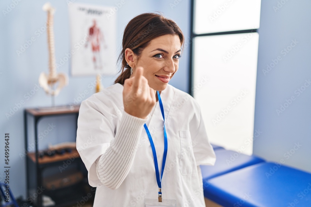 Young brunette woman working at pain recovery clinic beckoning come here gesture with hand inviting welcoming happy and smiling Young brunette woman working at pain recovery clinic beckoning come here gesture with hand inviting welcoming happy and smiling