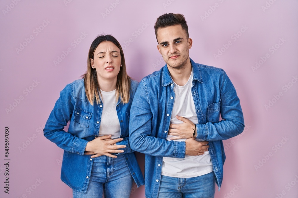Young hispanic couple standing over pink background with hand on stomach because indigestion, painful illness feeling unwell. ache concept. Young hispanic couple standing over pink background with hand on stomach because indigestion, painful illness feeling unwell. ache concept.