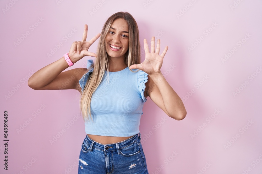 Young blonde woman standing over pink background showing and pointing up with fingers number eight while smiling confident and happy. Young blonde woman standing over pink background showing and pointing up with fingers number eight while smiling confident and happy.