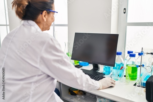 Middle age hispanic woman wearing scientist uniform using computer at laboratory