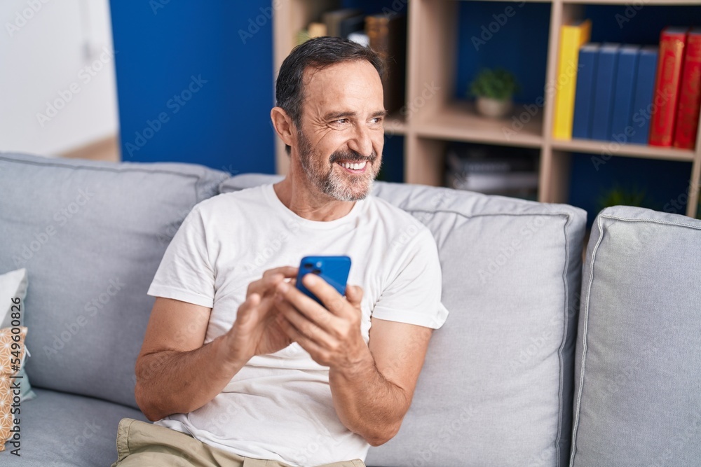 Middle age man using smartphone sitting on sofa at home Middle age man using smartphone sitting on sofa at home